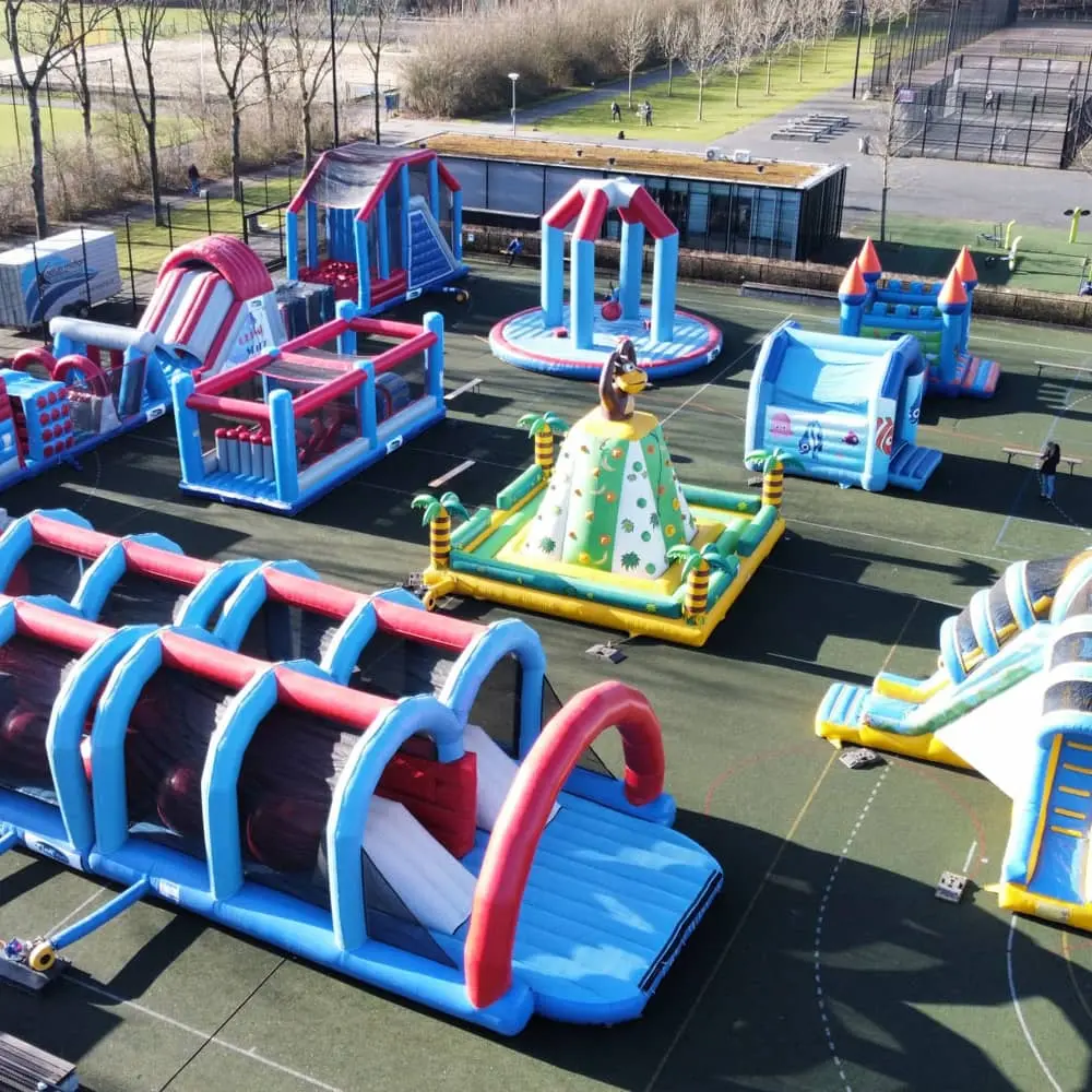 Groot buitenterrein vol kleurrijke stormbanen en springkussens, opgesteld op een sportveld tijdens een evenement